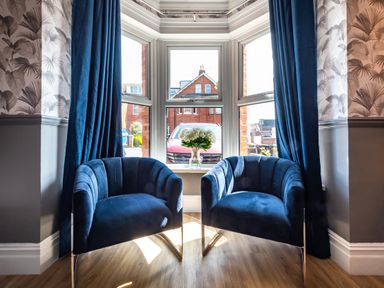 Two blue armchairs in front of a bay window with blue curtains and a vase of flowers at Anchor House in Weymouth