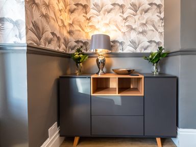 A grey sideboard with a lamp a bowl and two vases with flowers in a corner of a room at Anchor House in Weymouth