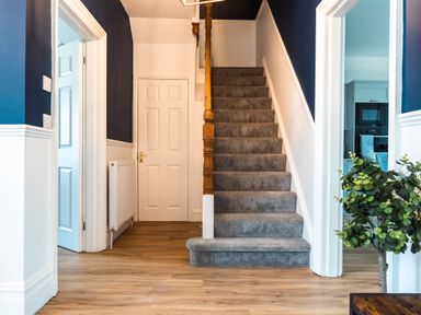 A hallway with carpeted stairs a wooden banister wooden floor blue and white walls two doorways and a plant at Anchor House in Weymouth