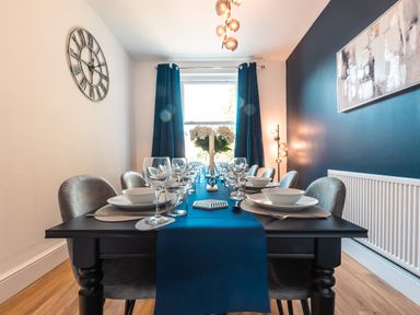 A dining room with a black table set with plates glasses and a blue table runner with chairs around at Anchor House in Weymouth