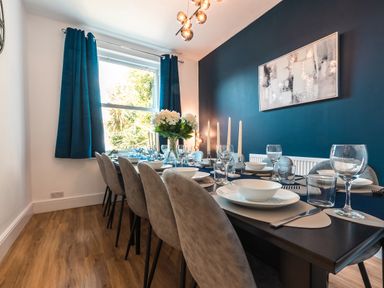 A dining room with a long table set with plates glasses and candles near a window with blue curtains at Anchor House in Weymouth