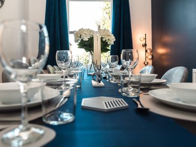 A dining table set with plates glasses candles and flowers in a room with blue curtains at Anchor House in Weymouth