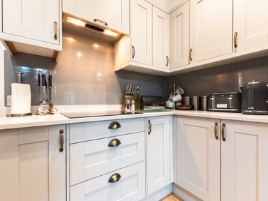 A kitchen with white cabinets a stovetop kitchen utensils a paper towel holder a knife set a toaster a kettle and mugs at Anchor House in Weymouth