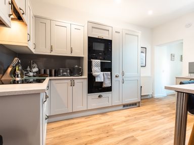 A kitchen with white cabinets black appliances and wooden floor at Anchor House in Weymouth
