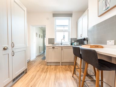 A kitchen with white cabinets a window and two bar stools at Anchor House in Weymouth