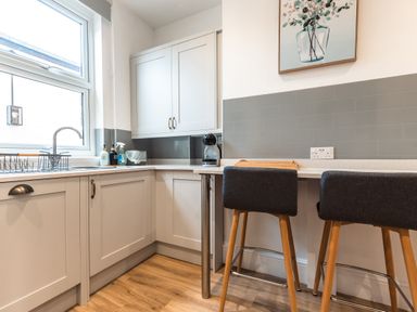A kitchen with white cabinets a countertop with soap dispensers a coffee machine two stools and a painting at Anchor House in Weymouth