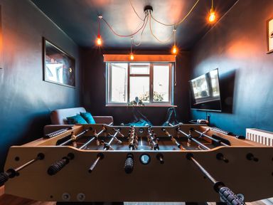 A game room with a foosball table a sofa a flat screen TV and hanging light bulbs at Anchor House in Weymouth