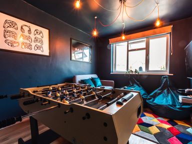 A game room with a foosball table, a sofa, bean bags by the window, and framed game controller art at Anchor House in Weymouth