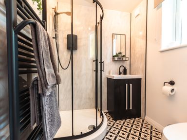 A bathroom with a curved glass shower enclosure a black vanity cabinet with a white sink a towel rack with towels and a patterned tile floor at Anchor House in Weymouth