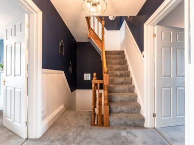 A carpeted staircase with wooden banisters between two doorways in a hallway with dark blue and white walls at Anchor House in Weymouth