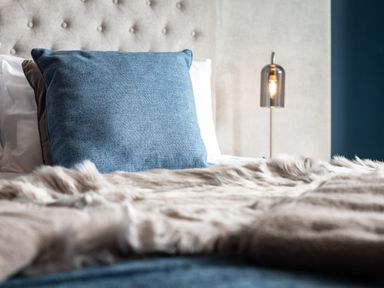 A bed with blue and white pillows a fur throw and a bedside lamp at Anchor House in Weymouth