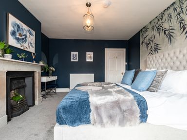 A bedroom with a large bed with blue and gray pillows a fireplace a small desk and blue walls at Anchor House in Weymouth