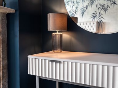 A table lamp on a white console table below a round mirror with a dark wall background at Anchor House in Weymouth