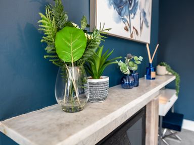 A marble mantle with green plants in pots and vases against a blue wall at Anchor House in Weymouth