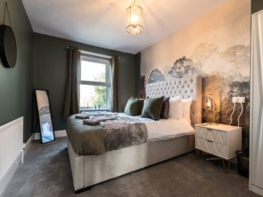 A bedroom with a bed green pillows a bedside table with a lamp and a wall mural at Anchor House in Weymouth