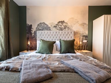A bedroom with a bed with green pillows gray towels on a fur throw and bedside tables with lamps at Anchor House in Weymouth