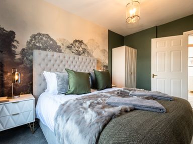 A bedroom with a large bed with pillows and blankets bedside table lamp a wardrobe and a door at Anchor House in Weymouth