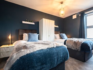 A bedroom with two single beds blue bedding a white wardrobe and window curtains at Anchor House Weymouth
