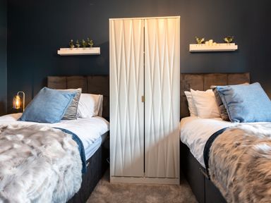 A bedroom with two single beds separated by a white wardrobe and shelves with small plants and candles at Anchor House in Weymouth