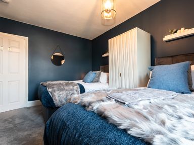 A bedroom with two beds blue pillows and blankets a white wardrobe and a round mirror on a dark wall at Anchor House in Weymouth