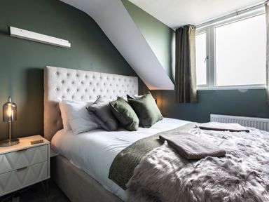 A bedroom with a bed with pillows and blankets next to a window and a nightstand with a lamp at Anchor House in Weymouth