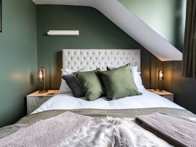 A bedroom with a tufted headboard green and gray pillows bedside tables with lamps and folded towels at Anchor House in Weymouth