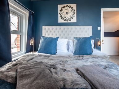 A bedroom with a bed with blue pillows and gray towels on a fur cover at Anchor House in Weymouth