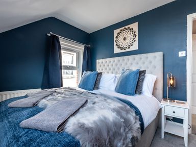 A bedroom with a bed with blue and gray bedding pillows and a nightstand with a lamp at Anchor House in Weymouth