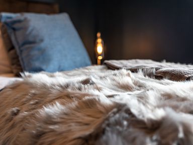 A bed with a furry blanket a blue pillow and a lamp in the background at Anchor House in Weymouth