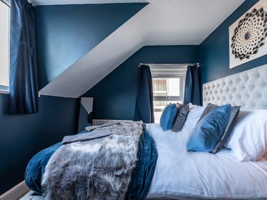 A bedroom with a bed with blue and gray pillows blue walls and two windows at Anchor House in Weymouth