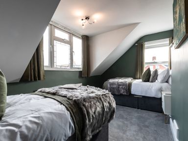 A bedroom with two beds, windows with curtains, and a nightstand at Anchor House in Weymouth
