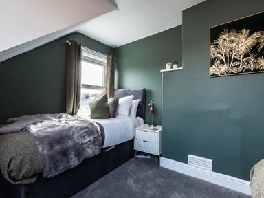 A bedroom with a bed next to a window a bedside table with a lamp and small plants on a shelf at Anchor House in Weymouth