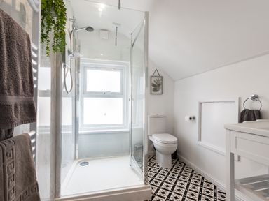 A bathroom with a shower enclosure a toilet patterned floor tiles and towels at Anchor House in Weymouth