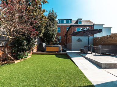 A backyard with artificial grass a hot tub outdoor seating with an umbrella and a brick house at Anchor House in Weymouth