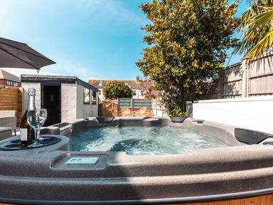 An outdoor patio with a hot tub a bottle of champagne and a glass two chairs under a tree at Anchor House in Weymouth