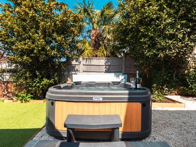 A hot tub with a bottle of wine and glasses in a garden with trees at Anchor House in Weymouth