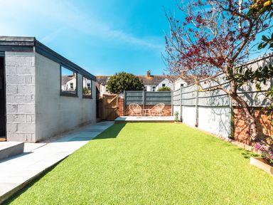 A backyard with artificial grass a tree a concrete path and two chairs at Anchor House in Weymouth
