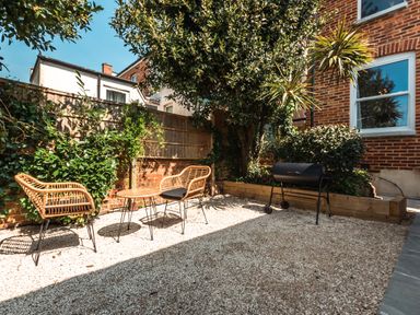 An outdoor patio area with two wicker chairs a small round table a barbecue grill and plants at Anchor House in Weymouth