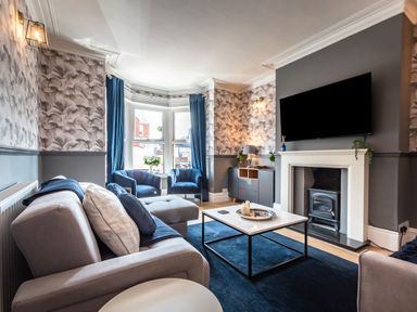 A living room with grey sofa blue chairs and a television above the fireplace at Anchor House in Weymouth