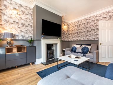 A living room with a grey sofa pillows a white coffee table a fireplace a TV wall cabinet and wooden floor at Anchor House in Weymouth