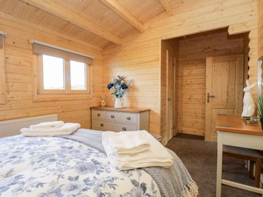 A bedroom with a bed towels on it a chest of drawers with flowers and a desk with a chair at Howgills Retreat in Gatebeck near Kirkby Lonsdale