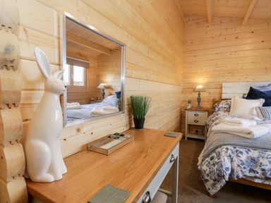 A bedroom with wooden walls a bed with floral bedding a bedside table with a lamp and a wooden desk with a ceramic rabbit and mirror at Howgills Retreat in Gatebeck near Kirkby Lonsdale