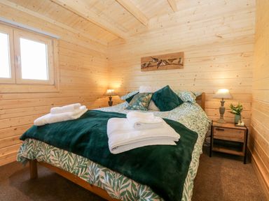 A bedroom with a bed covered in green and white bedding and folded towels on top at Howgills Retreat in Gatebeck near Kirkby Lonsdale