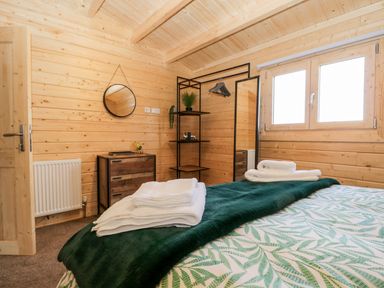 A bedroom with wooden walls a bed with folded towels a chest of drawers a mirror and a window at Howgills Retreat in Gatebeck near Kirkby Lonsdale