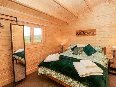 A bedroom with a double bed green bedding bedside tables lamps and a full length mirror at Howgills Retreat in Gatebeck near Kirkby Lonsdale