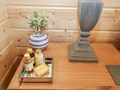 A wooden bedside table with a small striped vase plant toiletries on a mirrored tray and a lamp base at Howgills Retreat in Gatebeck near Kirkby Lonsdale