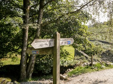 A wooden signpost on a dirt path with directions to Grasmere and Ambleside surrounded by trees and stone walls at Howgill Lodge in Gatebeck near Kirkby Lonsdale