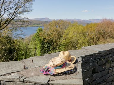 Two straw hats and sunglasses on a stone wall with trees and a lake in the background at Howgill Lodge in Gatebeck near Kirkby Lonsdale