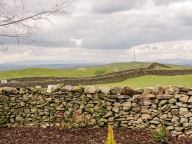Stone walls in a grassy rural landscape with hills and a communication tower in the background at Howgill Lodge in Gatebeck near Kirkby Lonsdale