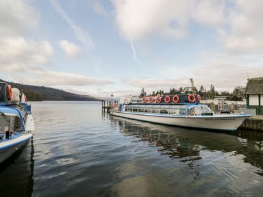 A passenger boat docked at a pier on a lake with hills in the background at Howgill Lodge in Gatebeck near Kirkby Lonsdale